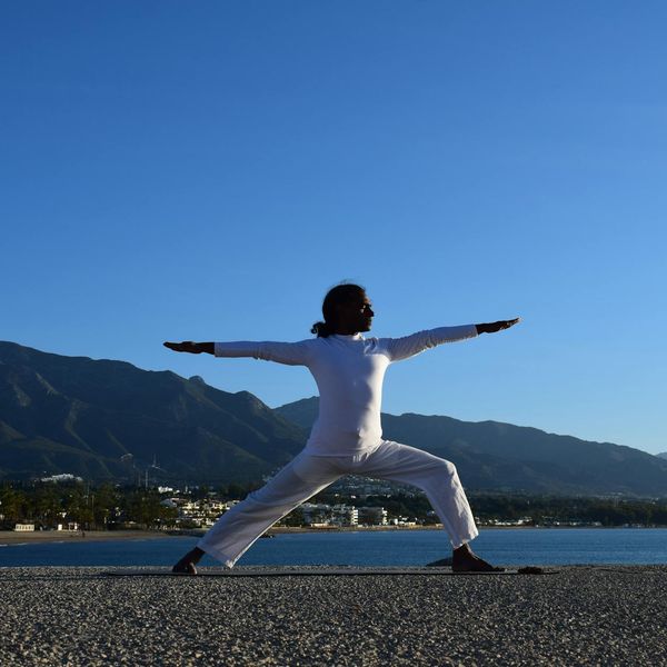 Silhouette of a person in a powerful warrior yoga pose against a sunrise.